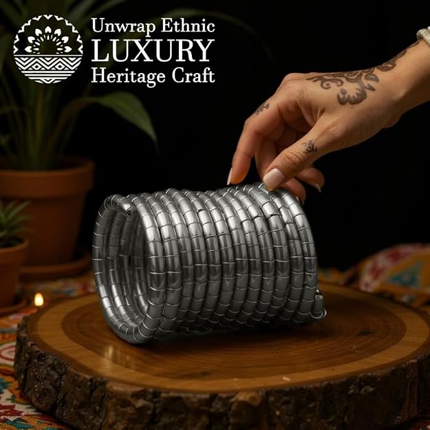 Set of silver-toned brass bangles in a coil style, shown stacked on a wooden surface, with a hand gently holding them.
